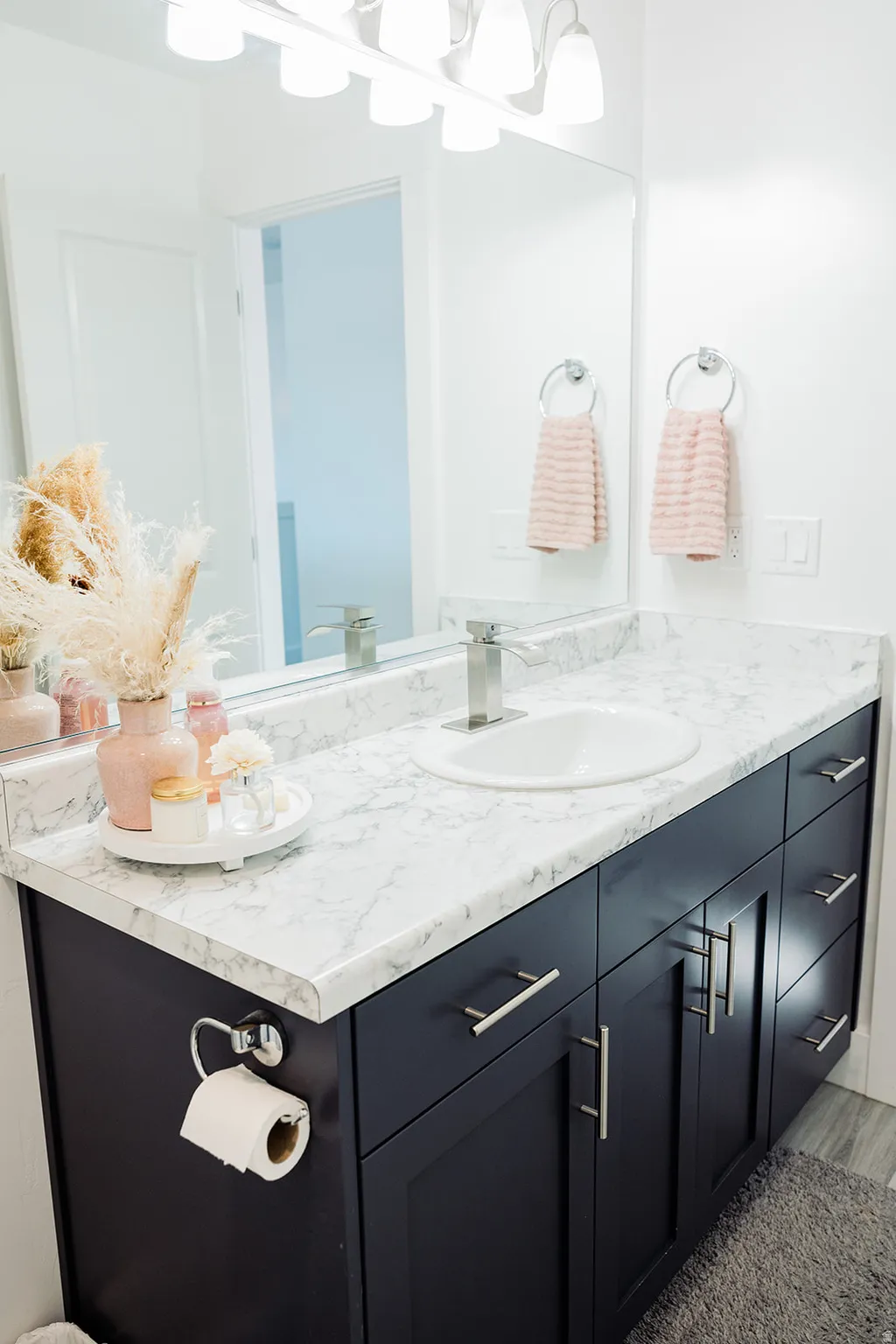 Vanity featuring dark cabinetry, a white countertop with grey veining, an integrated sink with a chrome faucet, and a large wall-mounted mirror