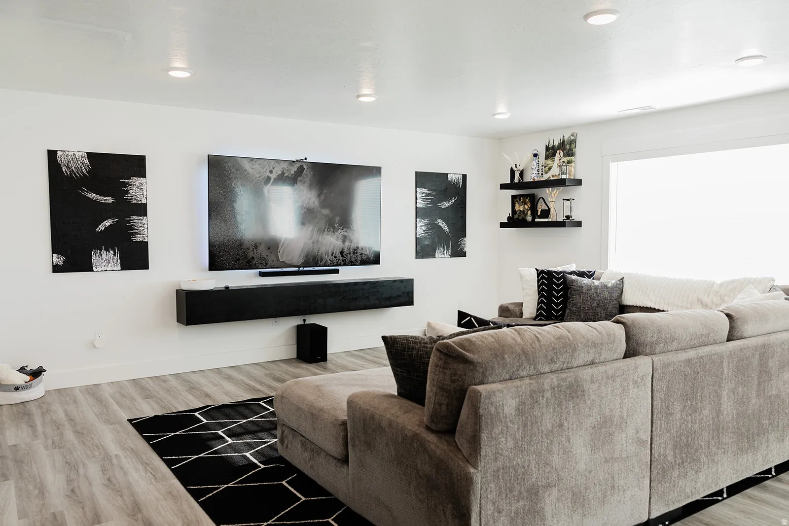 Spacious living area featuring light wood-finish flooring, recessed lighting, and a prominent built-in media console