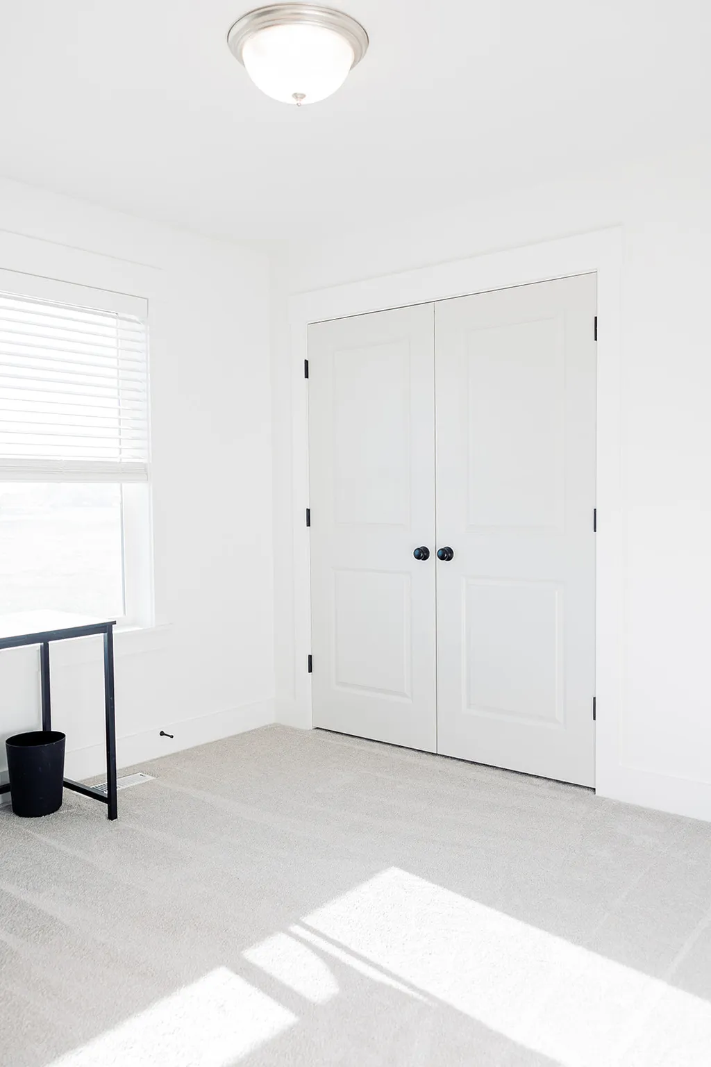 Neutral-toned carpeting extends throughout this interior space, featuring white walls and a window with horizontal blinds
