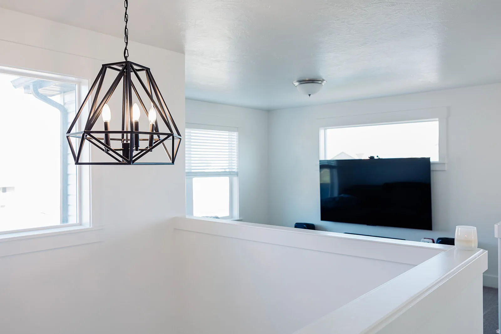 Modern geometric chandelier with three exposed bulbs, crisp white walls, white window trim, and a white half-wall
