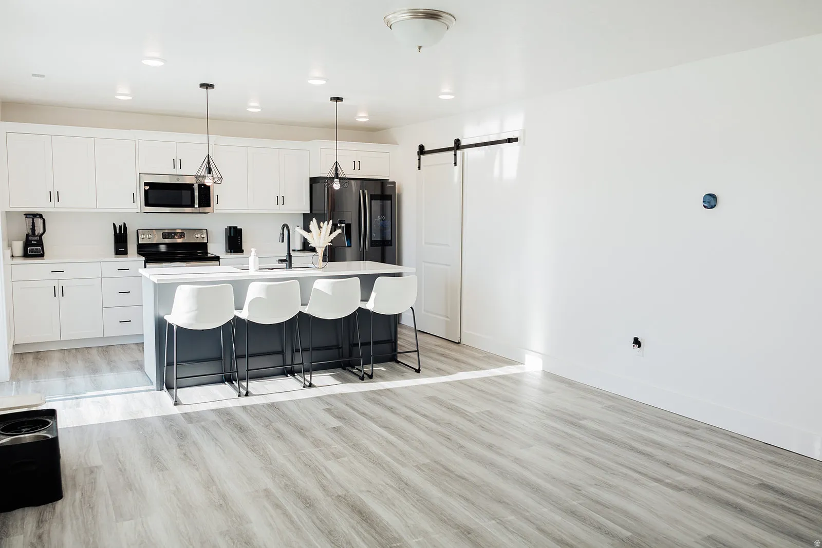Open-concept kitchen featuring white cabinetry, stainless steel appliances, a dark-toned island with integrated seating, and pendant lighting