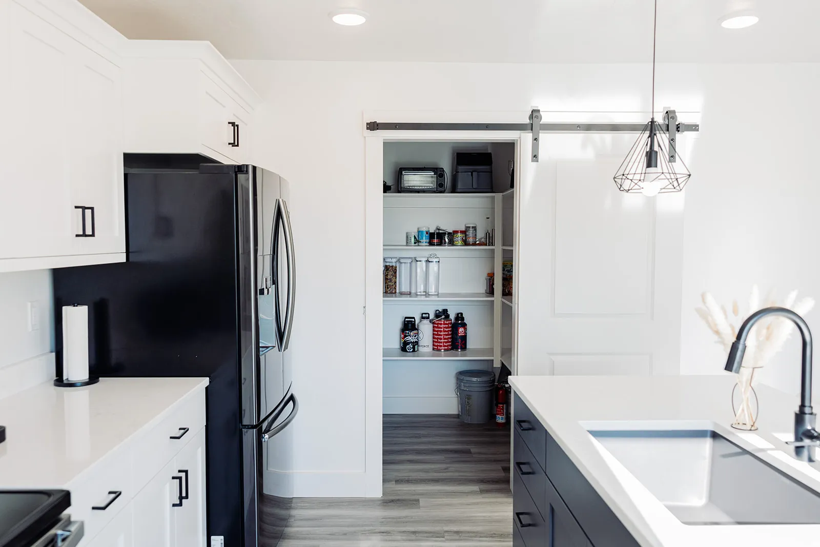 Modern kitchen featuring white shaker cabinetry, white countertops, black appliances, and a pantry with a sliding barn door