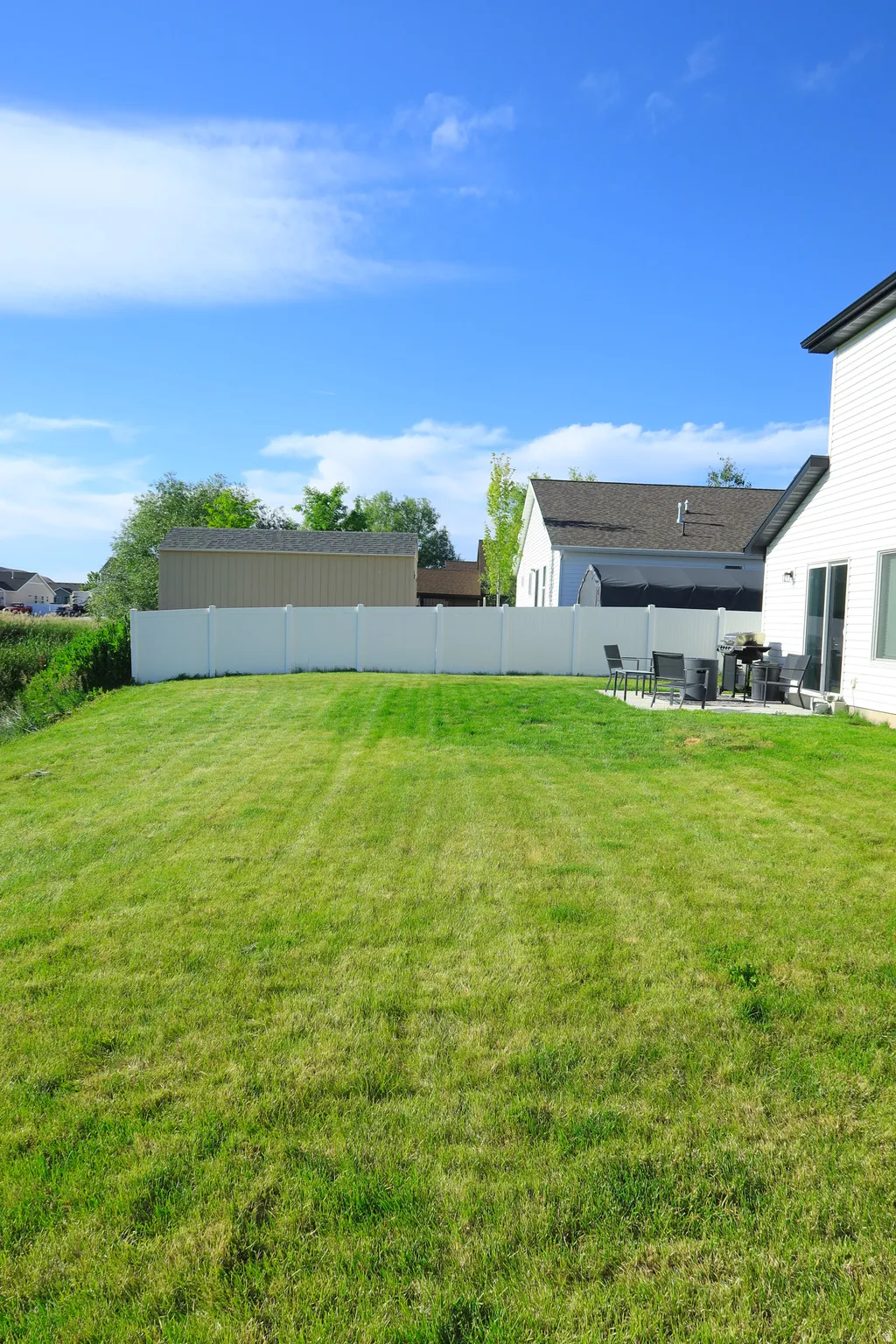Expansive green lawn with a white privacy fence, complemented by a concrete patio for outdoor enjoyment