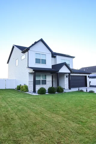 Contemporary two-story exterior featuring white vertical and horizontal siding, black trim accents, a two-car garage, and stone veneer detailing on the front facade