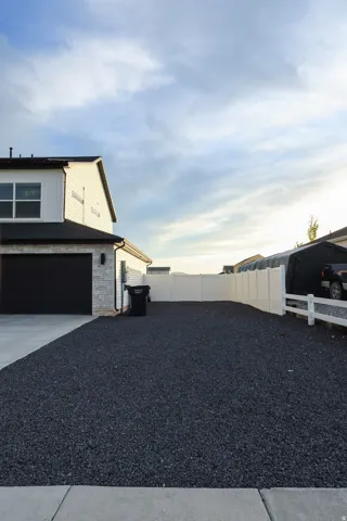 Modern siding facade with stone veneer accents, a dark garage door, and an expansive gravel side yard