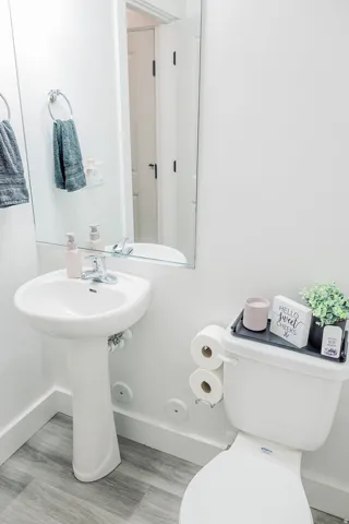 Pedestal sink with chrome faucet, large wall mirror, and grey wood-finish flooring