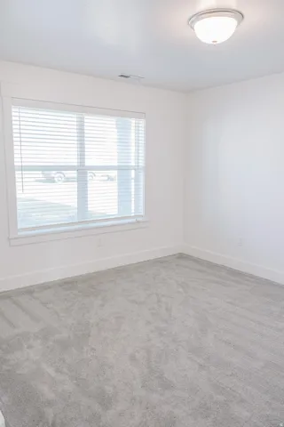 Bright interior space featuring a window with horizontal blinds, neutral wall paint, white trim, and light grey carpet flooring