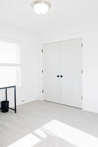Neutral-toned carpeting extends throughout this interior space, featuring white walls and a window with horizontal blinds