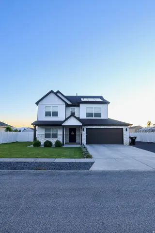 Modern farmhouse exterior featuring black trim, white vertical and horizontal siding, stone veneer accents, a dark garage door, and solar panels