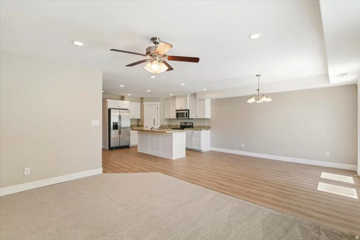 Open-concept living space featuring a partial carpet and wood-finish flooring, recessed lighting, and a ceiling fan