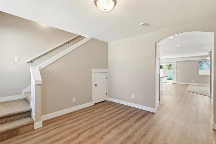 Entry area featuring wood-finish flooring, a carpeted staircase with white railing, and an arched entryway leading to an open concept living space