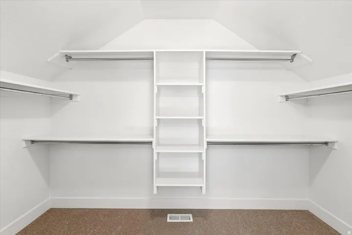 Spacious closet featuring white built-in shelving, multiple hanging rods, and an integrated central storage unit