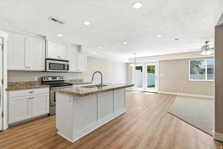 Open-concept kitchen featuring white shaker cabinetry, stainless steel appliances, and a central island with a sink