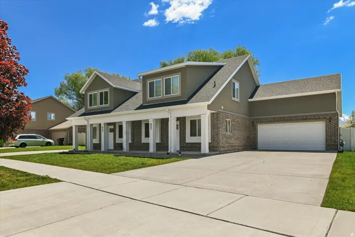Two-story residence featuring a brick and stucco exterior, white columned front porch, multi-pane windows, attached two-car garage, and concrete driveway