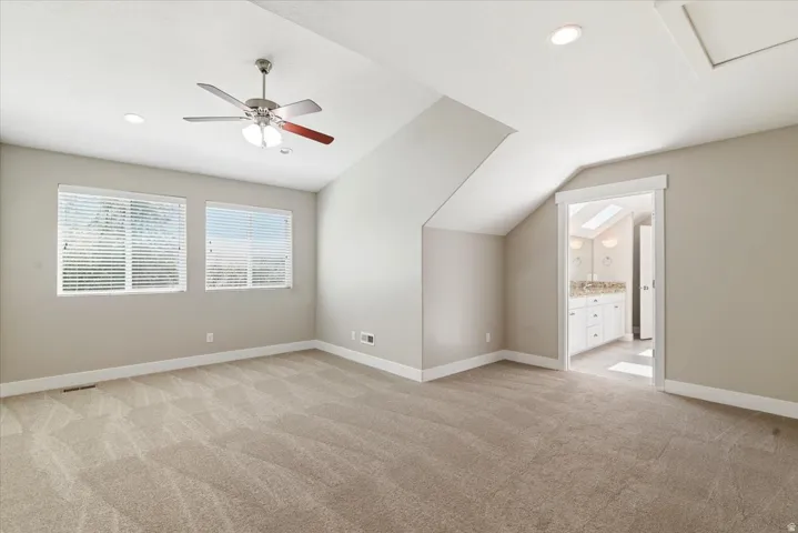 Spacious room featuring vaulted ceilings, recessed lighting, neutral-toned carpeting, a ceiling fan, and two windows with horizontal blinds
