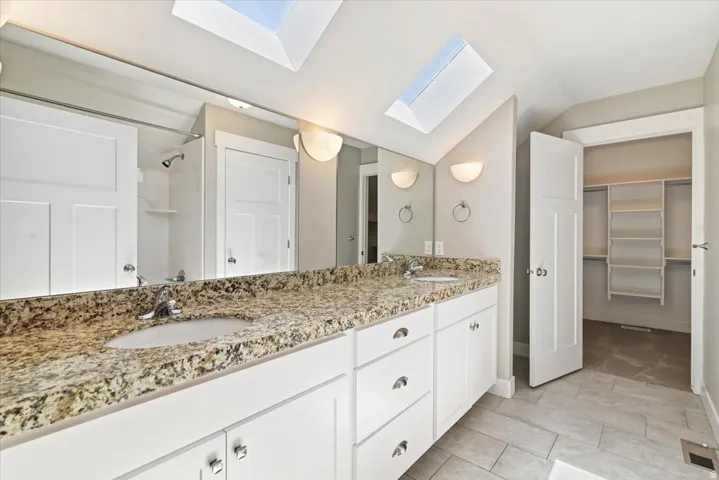 Master bath. Dual vanity with granite countertop, white cabinetry, and skylights