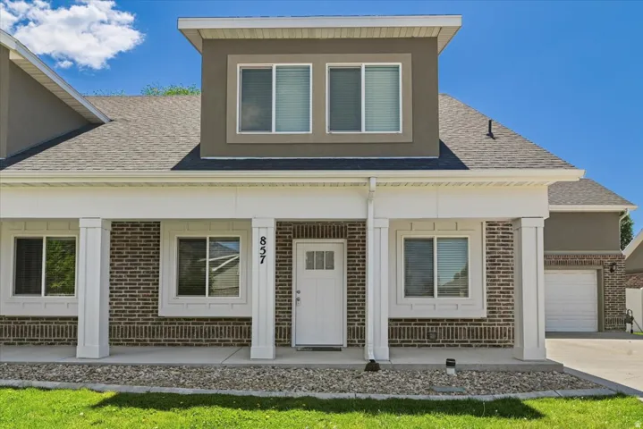 Modern exterior featuring brick and stucco siding, a covered front porch with white columns, and a prominent second-story dormer
