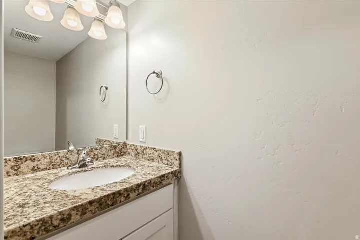 Bathroom vanity with a granite countertop, undermount sink, and chrome faucet