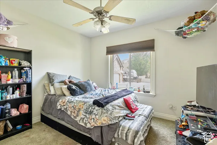 Carpeted room featuring a window with a roller shade, a ceiling fan with light fixture, and a built-in bookshelf