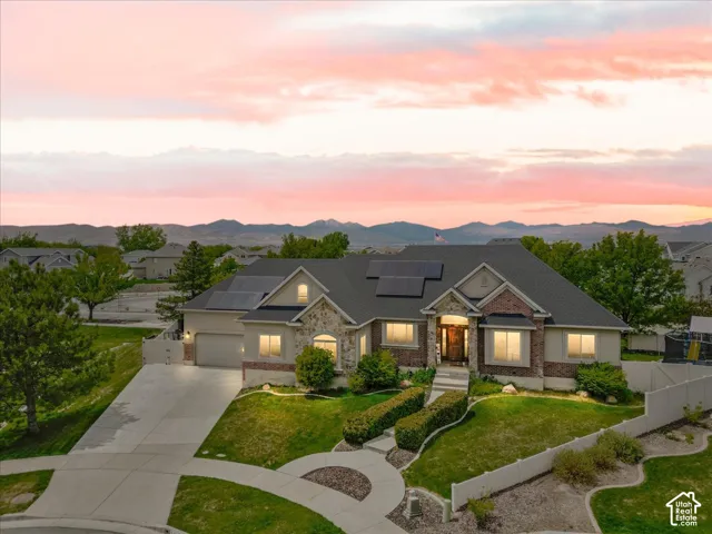 Exterior featuring a stone and brick facade, a multi-car driveway, a covered entry, a dark roof with solar panels, and mature landscaping