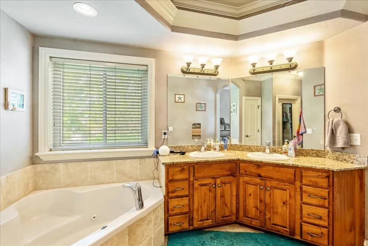 Corner jetted tub with tile surround, complemented by a dual vanity featuring wood cabinetry and a speckled countertop