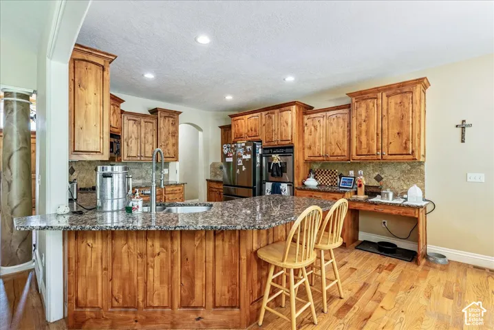 Kitchen featuring a large central island with seating, natural wood cabinetry, granite countertops, stainless steel appliances, and wood-finish flooring