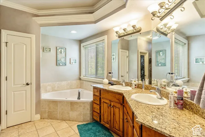 Double vanity with granite countertop and integrated sinks, corner soaking tub with tiled surround, wood cabinetry, and crown molding details