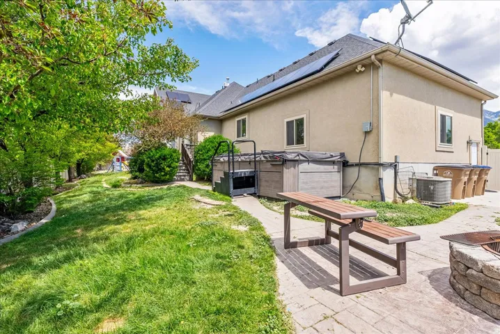Expansive backyard featuring a lush lawn, mature trees, and a paver patio with a built-in fire pit