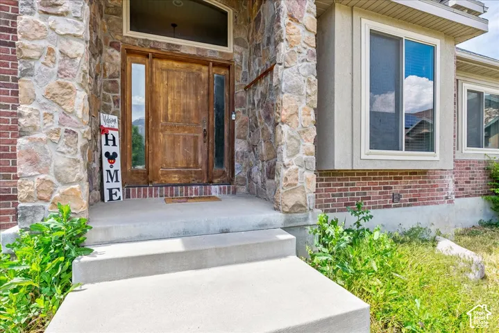 Exterior featuring a natural wood entry door with side windows, stone column accents, and a complementary brick facade