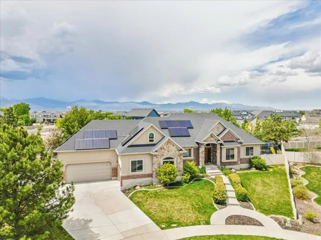 Spacious residence featuring a multi-gabled roofline with solar panels, a stone and brick facade, an attached garage, and a concrete driveway