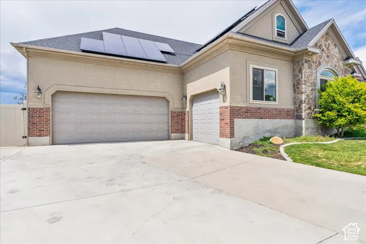 Stucco and stone exterior featuring a two-car garage, single-car garage, and solar panels