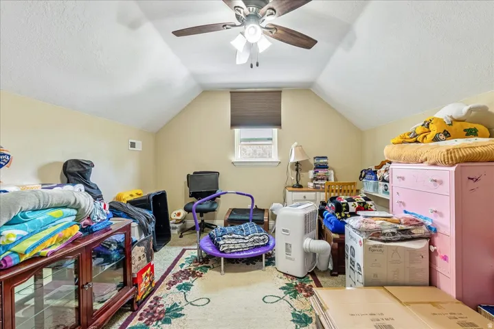Attic room featuring a sloped ceiling, central ceiling fan, light beige wall paint, and a window with a dark window treatment
