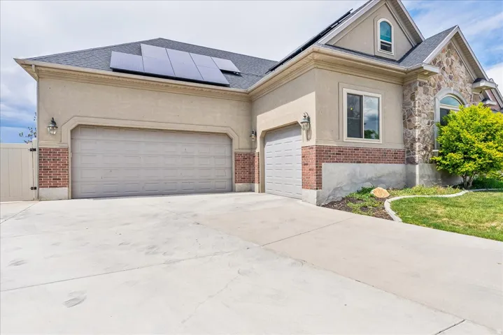 Stucco and stone exterior featuring a two-car garage, single-car garage, and solar panels