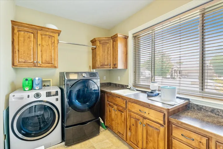 Dedicated laundry space featuring wood cabinetry, a utility sink, ample counter space, a clothing rod, and window with blinds