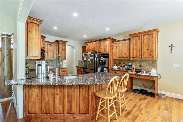 Kitchen featuring a large central island with seating, natural wood cabinetry, granite countertops, stainless steel appliances, and wood-finish flooring