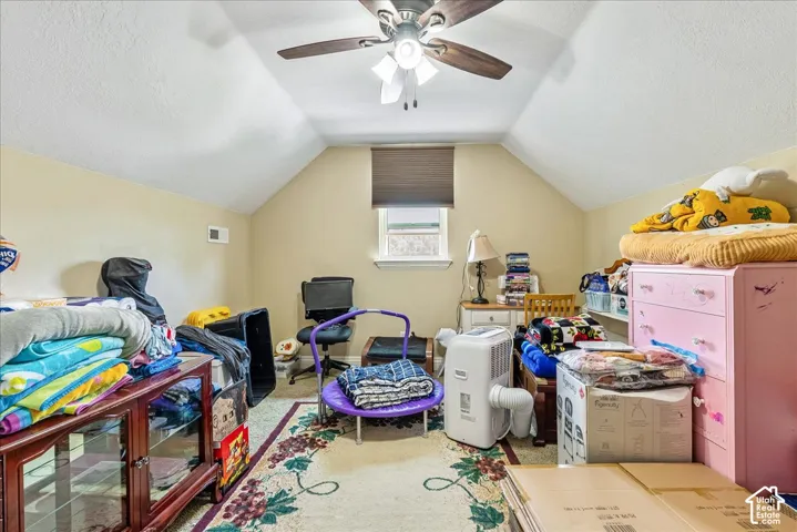 Attic room featuring a sloped ceiling, central ceiling fan, light beige wall paint, and a window with a dark window treatment