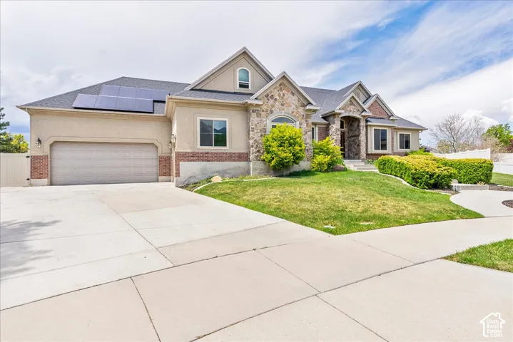 Stucco and stone exterior featuring a two-car garage, solar panels, and a concrete driveway