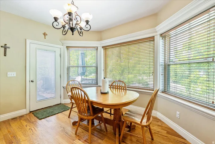 Bay window with multiple windows, wood-finish flooring, a white-framed door with a frosted glass panel, and a decorative chandelier