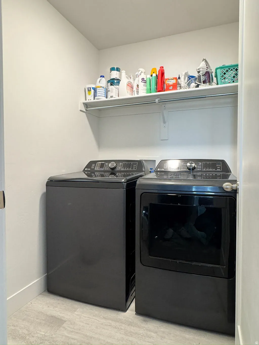 Dedicated laundry area featuring a white wire shelf, light-toned walls, and grey tile flooring