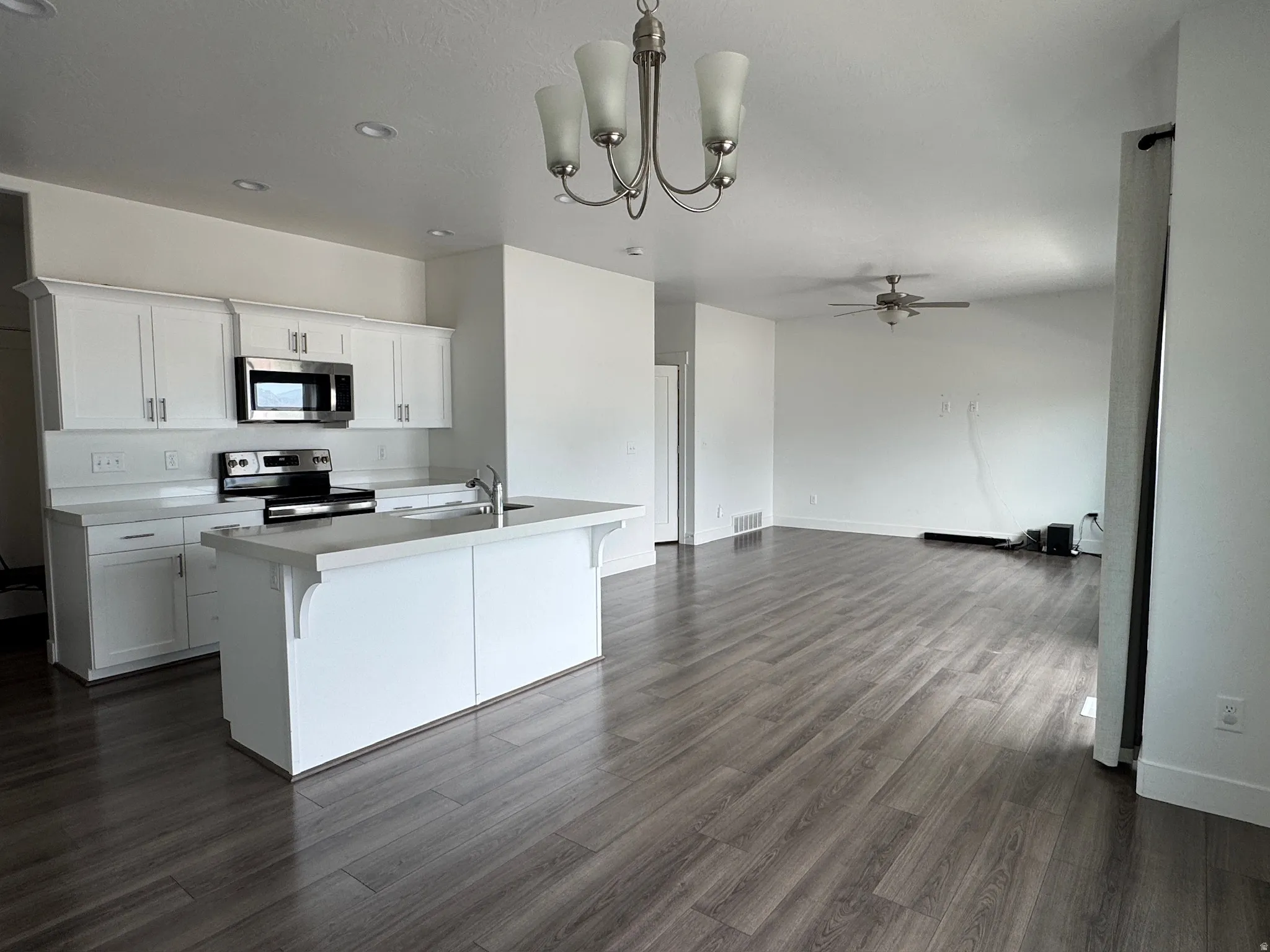 Open-concept living space featuring a modern kitchen with white cabinetry, stainless steel appliances, and a central island with a sink