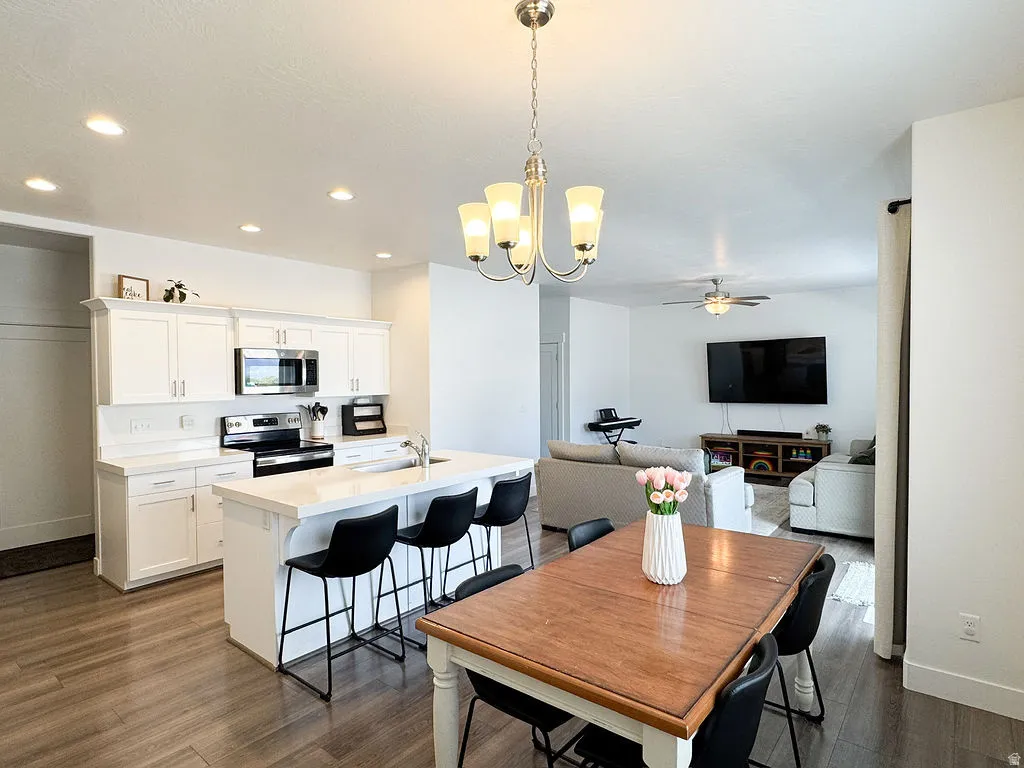 Open-concept living space featuring a kitchen with white cabinetry and stainless steel appliances, a center island with seating, wood-finish flooring, and a dining area with chandelier lighting
