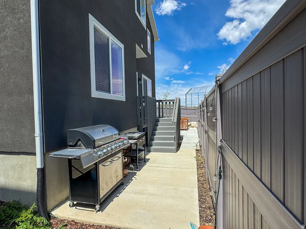 Exterior pathway featuring concrete paving, a dark-toned privacy fence, and an elevated wooden deck with stairs
