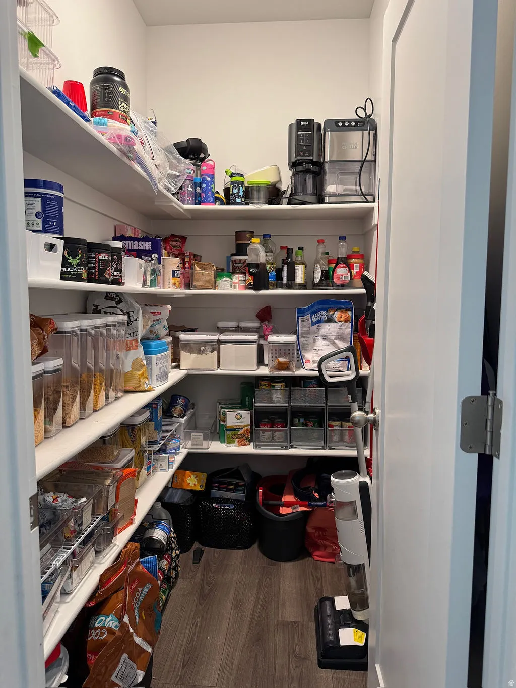 Walk-in pantry featuring white shelving, wood-finish flooring, and a white interior door