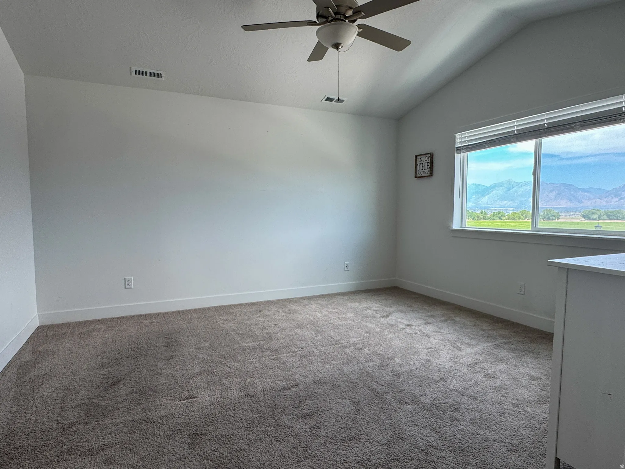 Spacious room featuring vaulted ceilings, a ceiling fan, plush carpeting, and a large window with mountain scenery