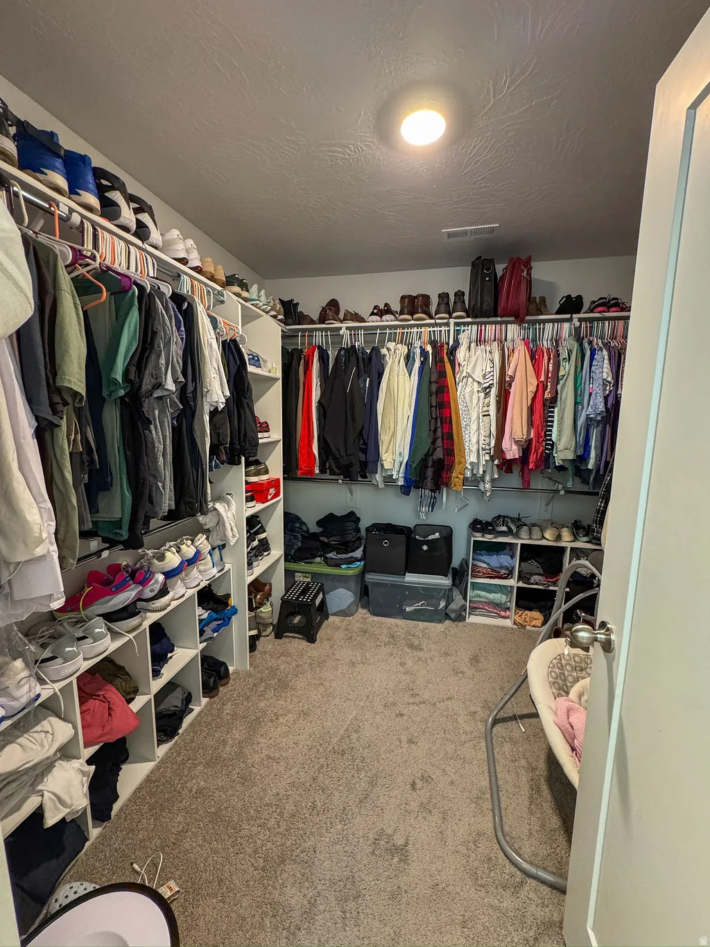 Spacious walk-in closet featuring extensive built-in shelving, multiple hanging rods, overhead storage, and soft carpeting
