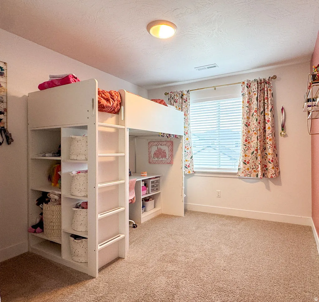 Neutral-toned carpeting extends throughout the room, complemented by a single window featuring blinds and decorative curtains