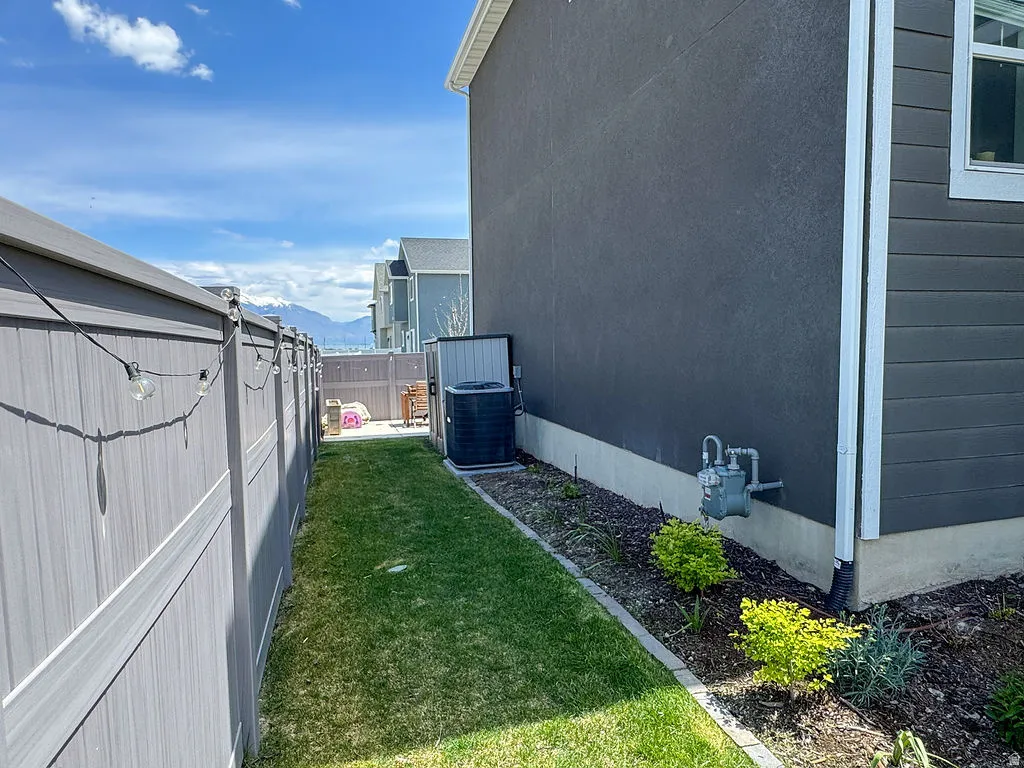 Fenced side yard with a manicured lawn, established landscaping, and a stucco and siding exterior