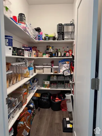 Walk-in pantry featuring white shelving, wood-finish flooring, and a white interior door