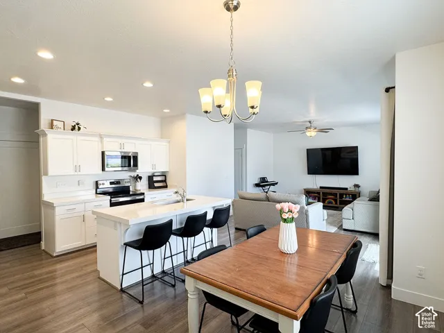Open-concept living space featuring a kitchen with white cabinetry and stainless steel appliances, a center island with seating, wood-finish flooring, and a dining area with chandelier lighting
