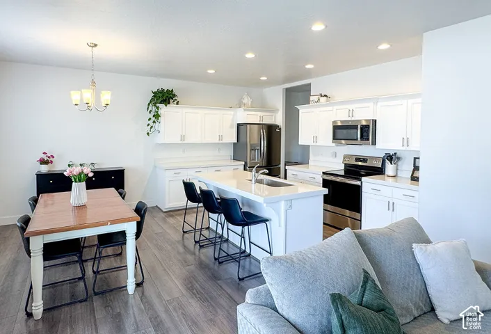 Open-concept living space featuring a kitchen with white cabinetry, stainless steel appliances, a center island with seating, and wood-finish flooring